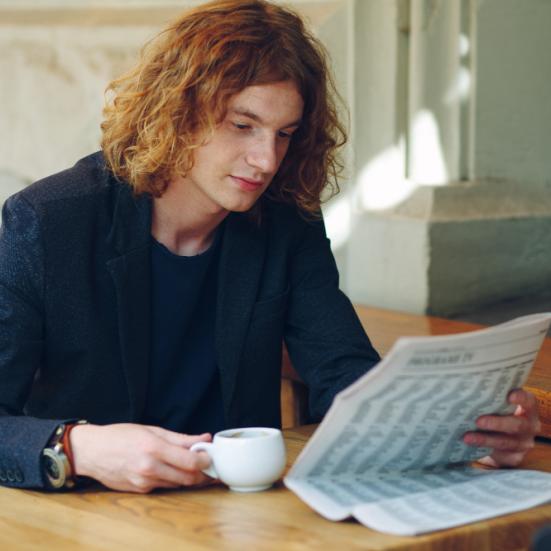 Mand, der sidder på en café og læser en avis, mens han drikker en kop kaffe.