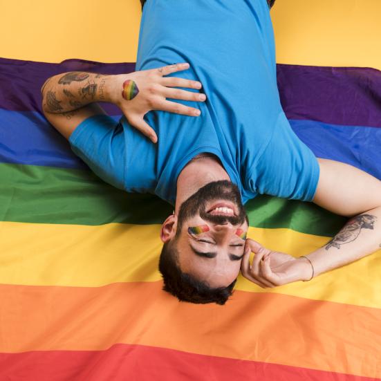 En smilende man, der ligger ovenpå et regnbueflag.