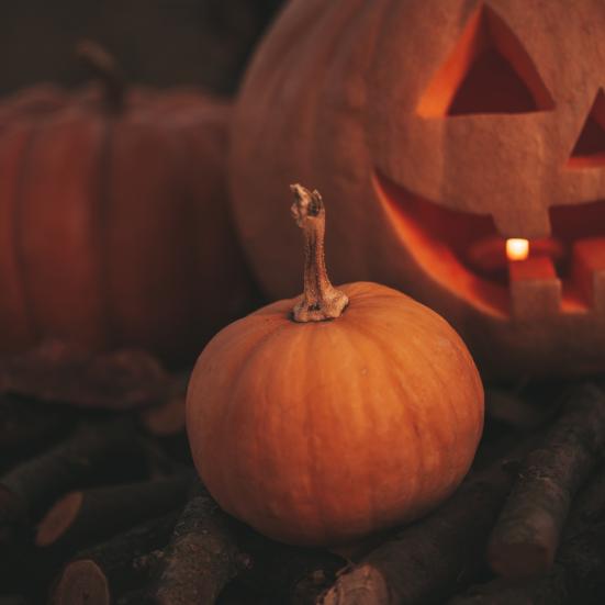 Græskar, der ligger på noget brænde. Et af dem er skåret som et klassisk Halloween-ansigt.