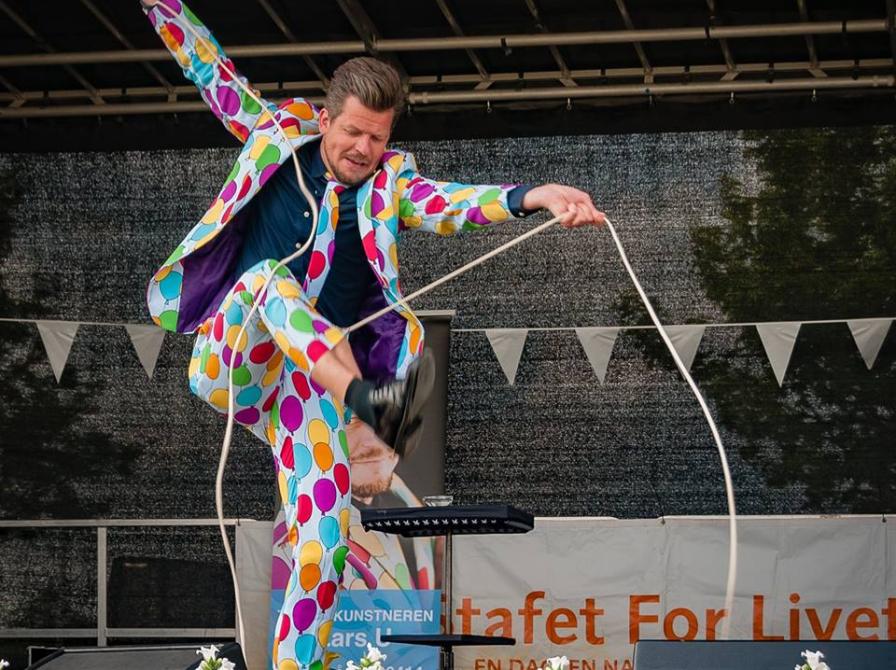 En mand i farverigt jakkesæt optræder på en scene. 